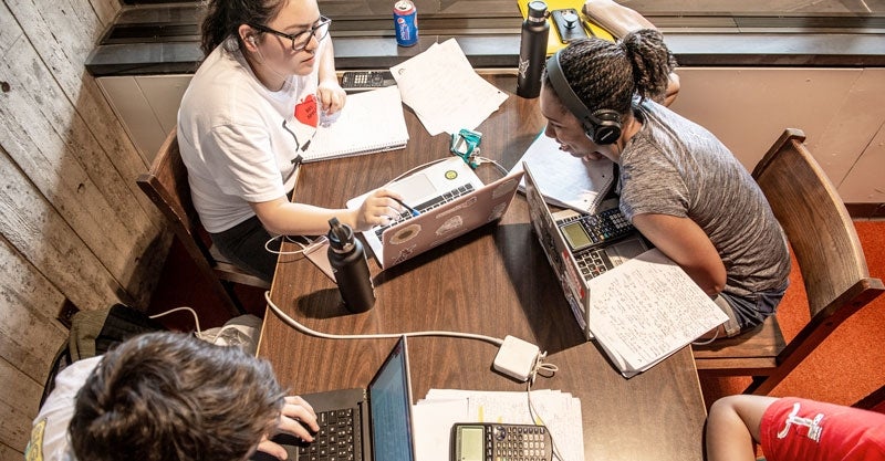 Two girls working at laptops in the library