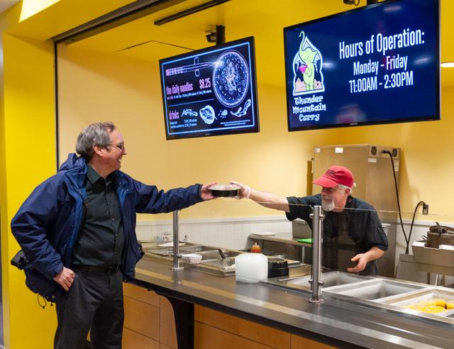 Chef at Thunder Mountain Curry hands lunch to a professor