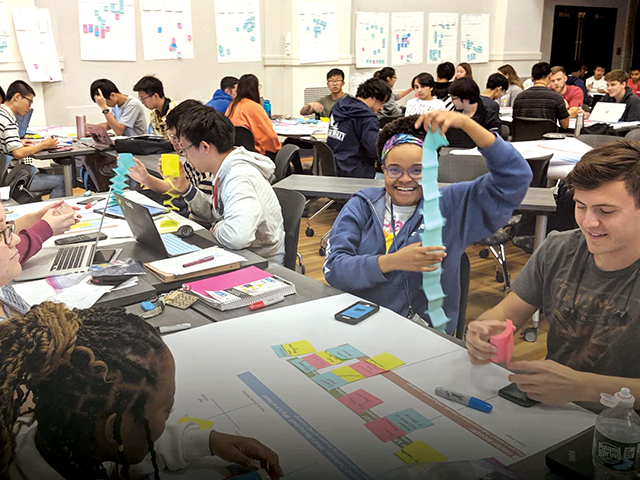 Student holding up her work and smiling, surrounded by other students